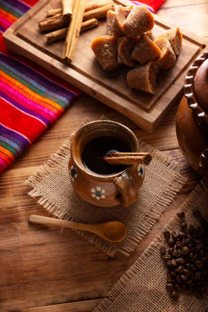 Coffee pot. Traditional Mexican coffee and basic ingredients for its preparation, coffee, cinnamon and piloncillo, served in a clay cup called "jarrito" on a rustic wooden surface.の写真素材