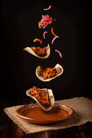 Creative food image of Mexican Tacos de Cochinita Pibil and onion with habanero chili falling on traditional mexican clay dish. Levitation photography.の写真素材