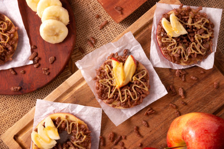 Creative party snack for holidays. Apple rounds with peanut butter, caramel and chocolate flavor puffed rice topping with banana slices. Funny appetizer for kids and adults.の写真素材