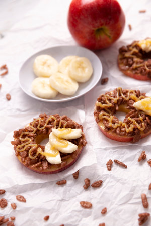 Creative party snack for holidays. Apple rounds with peanut butter, caramel and chocolate flavor puffed rice topping with banana slices. Funny appetizer for kids and adults.の写真素材