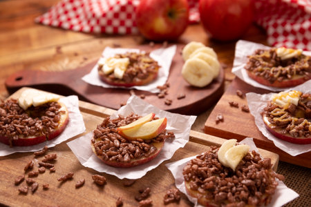 Creative party snack for holidays. Apple rounds with peanut butter, caramel and chocolate flavor puffed rice topping with banana slices. Funny appetizer for kids and adults.の写真素材