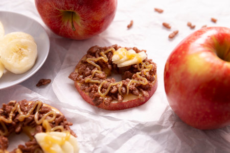Creative party snack for holidays. Apple rounds with peanut butter, caramel and chocolate flavor puffed rice topping with banana slices. Funny appetizer for kids and adults.の写真素材