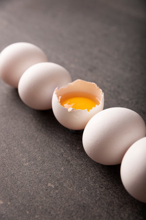White chicken eggs and egg yolk in a row on black stone table. Very popular nutritious and economic...