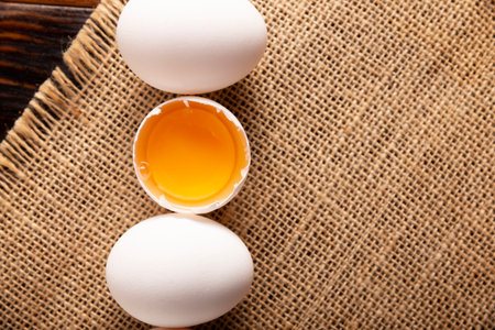 Chicken eggs and half broken egg with yolk on rustic table. Very popular nutritious and economic...