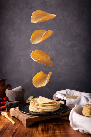 Corn tortillas falling on a Mexican griddle in a typical Mexican cuisine setting with a rustic wooden table and stone molcajetes.の写真素材