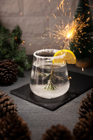 Snow Globe Cocktail. Christmas drink, creative festive beverage in drink glass decorated with rosemary sprig like a Christmas pine tree, citrus slice and Christmas sparkler.の写真素材
