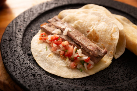 Arrachera tacos. Homemade grilled meat in a wheat tortilla served on a volcanic lava plate. Street food from Mexico, traditionally accompanied with cilantro, onion and spicy sauce or guacamole.の写真素材
