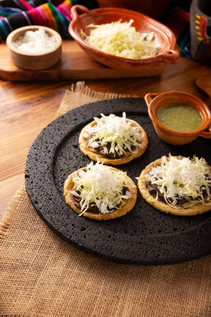 Sope. Traditional homemade Mexican food prepared with flattened and pinched on the border fried corn dough covered with refried beans, green or red sauce, cheese, onion and creamの写真素材