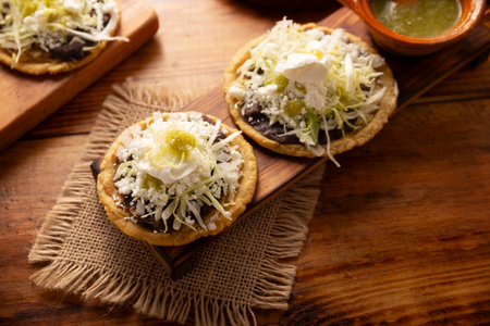 Sope. Traditional homemade Mexican food prepared with flattened and pinched on the border fried corn dough covered with refried beans, green or red sauce, lettuce, cheese and creamの写真素材