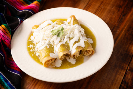 Green enchiladas. Typical Mexican dish made with a folded or rolled corn tortilla filled with shredded chicken and covered with spicy green sauce, cream, grated cheese and onion.の写真素材