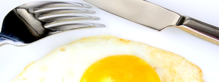 Fried egg with  fork and knife on a white backgroundの写真素材