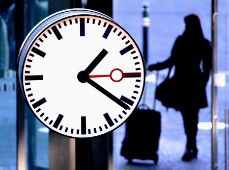 Station clock and a passenger waiting with suitcase の写真素材