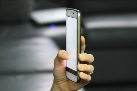 Holding smart phone in hand with blank white screenの写真素材