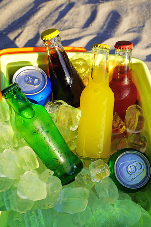 Colorful soda drinks and filled ice cubes in a coolbox on the beach sand.の写真素材
