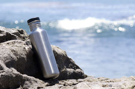 Stainless steel water bottle resting on a rock overlooking the ocean.の写真素材