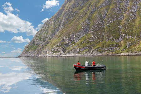 Two fisherman are fishing from a boat on the background of beautiful sceneryの写真素材