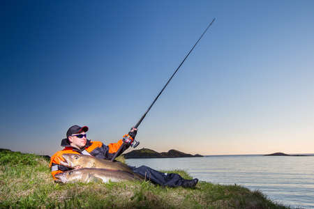 fisherman man sits on the shore. In the hands of a fishing rod spinning and with a huge fish....