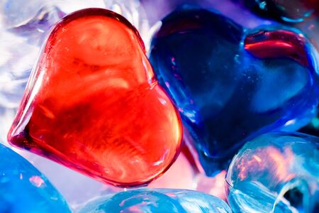 A big red heart and blue heart consisting of small multi-colored glass hearts on a blue background.の写真素材