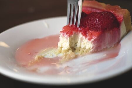 Fork breaks off a slice of juicy tasty strawberry pie. iron fork. white plate.