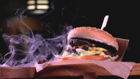 The hamburger is served on a rustic wooden surface and craft paper surrounded by smoke
