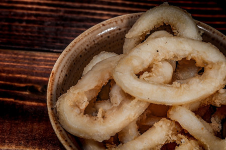 fried onion rings. Paper envelope, wooden table. Close-up.