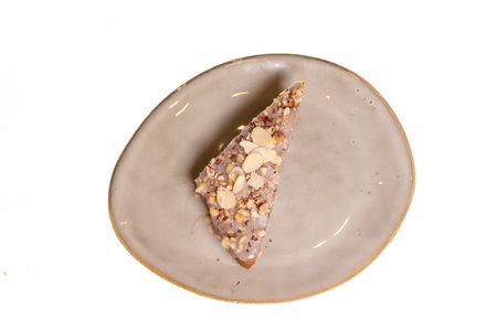 A slice of dark chocolate cake with a nutty topping is served on an ornate beige plate. Close-up side view.の写真素材