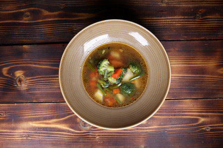 Vegetable soup is shown in a bowl on a wood table from an overhead shot.の写真素材