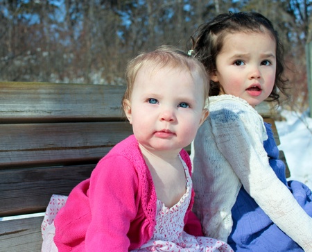 Two beautiful sisters sitting on benchの写真素材