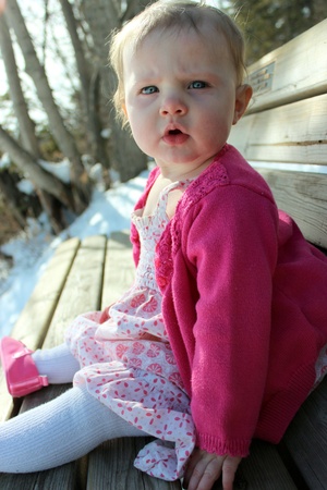 Adorable baby girl sitting on benchの写真素材