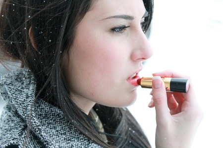 Beautiful woman applying lipstick outsideの写真素材