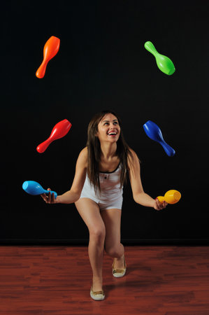 Beautiful young woman playing with colorful bowling clubs, isolated on black backgroundの写真素材