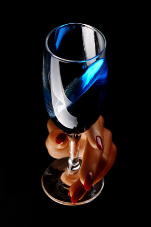 Female hand holding a glass of blue wine on a black background.の写真素材