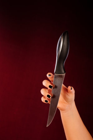 Female hand holding a kitchen knife on a dark red background close upの写真素材