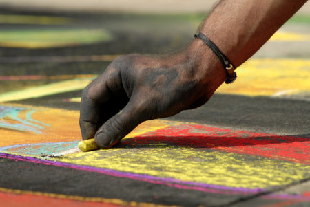 An artist hand at work making beautiful works of art on the street using soft pastel chalk while...