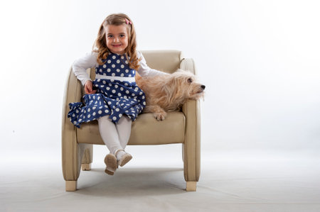 Little girl with her dog sitting in a chair on a white backgroundの写真素材