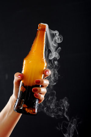 Female hand with a bottle of beer on a black background with smokeの写真素材