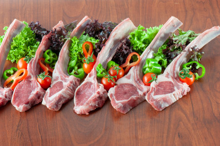 Raw lamb chops with fresh vegetables on a wooden table. Top view.の写真素材