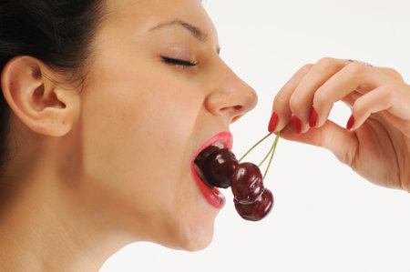 Close-up of young woman eating cherries on white background.の写真素材