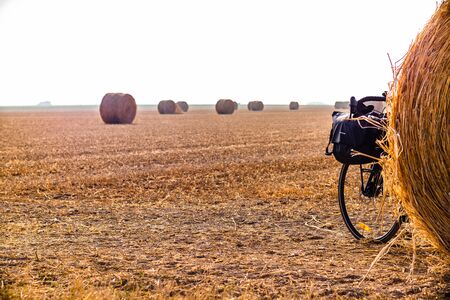 Touring bike hidden behind a hay ball in a big orangee-colored fieldの写真素材