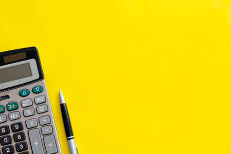 Flat lay or top view of pen with calculator on vivid yellow background table with blank copy space,...