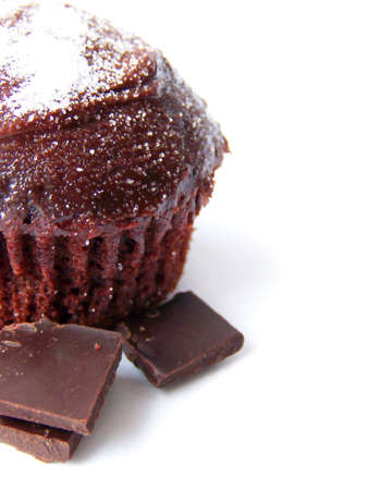 Image of an iced chocolate cupcake with granulated white sugar and pieces of dark chocolate, set to the left of the image.  Space remains for text or other material to the right.  Vertical orientation and white background.の写真素材