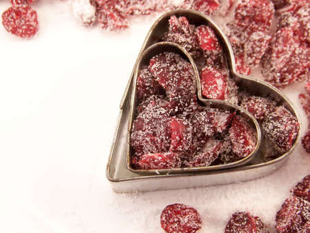 Image of dried cranberries mixed with white granulated sugar, placed within two different sized heart-shaped metal cookie cutters.の写真素材