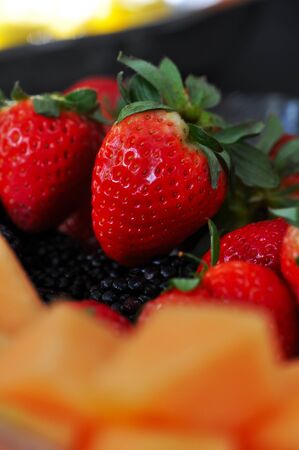 Close up photograph of red strawberries, orange melon and blackberries, together.の写真素材