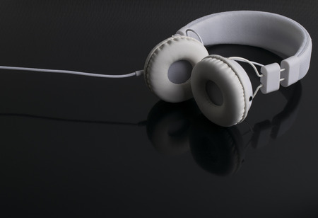 Isolated modern white headphone on a black reflected background.
