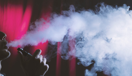 young person smoking and vaping electronic cigarette on a dark red background.の写真素材
