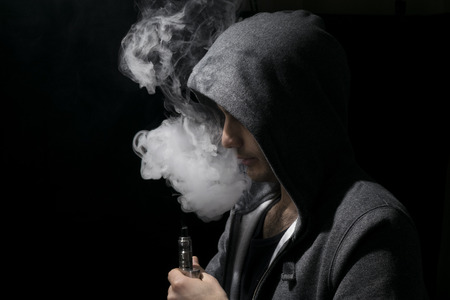 Man with hoody vaping an ecig, electronic cigarette.