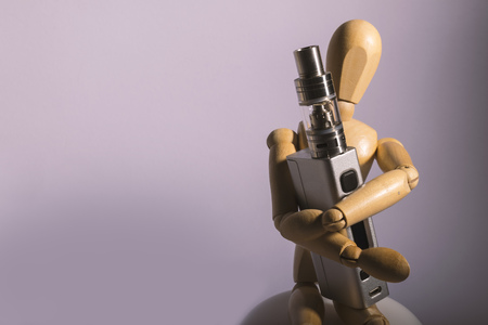 vape device hold by a wooden dummy over a white background.