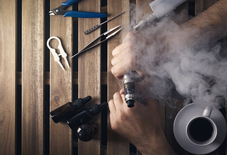 user holding by hands an electronic cigarette, vaping device top view, overhead view of e cigarette, e liquid, vape tools.の写真素材