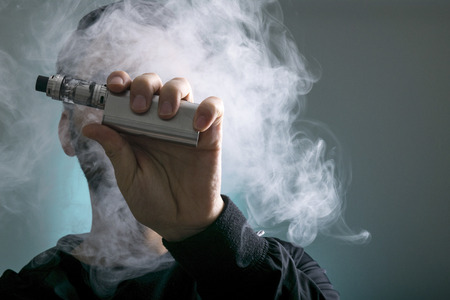 young man vape electronic cigarette cloud by using a mod, smoke tricks of vaping device background.