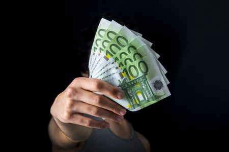 holding 100 euro money, hand holding one hundred euro cash isolated on a black backgroundの写真素材